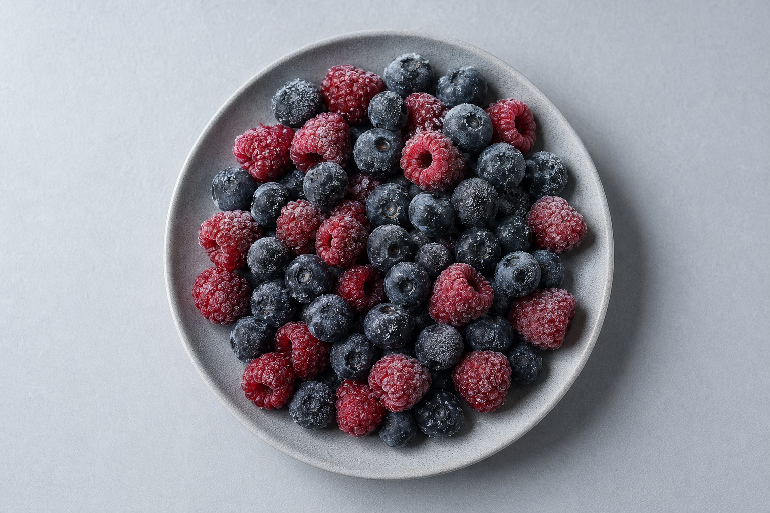 俯拍盘装冷冻浆果（蓝莓与树莓）表面薄霜清晰，深色浆果与霜面高对比的冷调主图